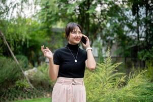 A positive, beautiful Asian woman talking on the phone while walking in a beautiful green garden. photo