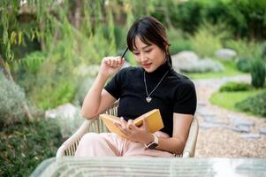 A positive Asian woman relaxing in a backyard and reading a book or writing her diary at a table. photo