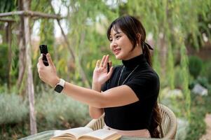 A cheerful Asian woman is talking on a call on her smartphone while relaxing in a garden. photo