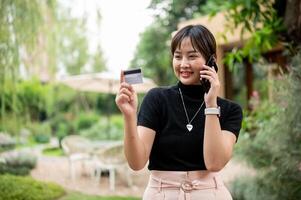 An Asian woman is calling her credit card or debit card call center while walking in a garden. photo