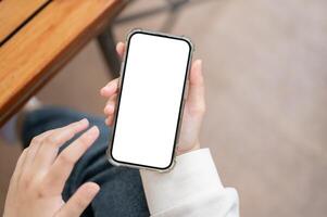 A close-up image of a woman in casual clothes using her smartphone at a table indoors. photo