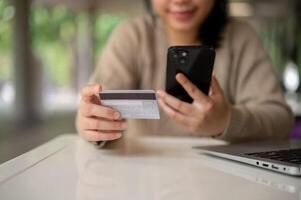 un joven contento asiático mujer utilizando su móvil bancario aplicación mientras sentado a un mesa adentro. foto