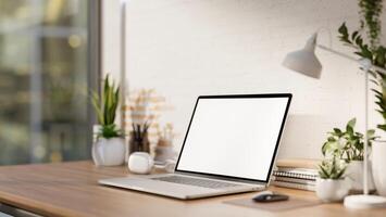 A minimalist workspace features a laptop computer mockup on a desk against the white brick wall. photo