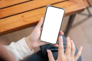 A close-up image of a woman in casual clothes using her smartphone at a table indoors. photo