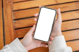 Top view image of a woman's hand holding a white-screen smartphone mockup over a wooden table. photo