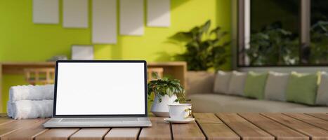 un pantalla blanca ordenador portátil computadora Bosquejo en un de madera mesa en un moderno verde vivo habitación. foto