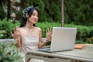 Beautiful Asian woman is having an online meeting with her colleagues, working remotely in a garden. photo