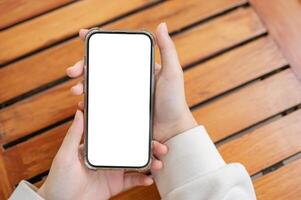 Top view image of a woman's hand holding a white-screen smartphone mockup over a wooden table. photo