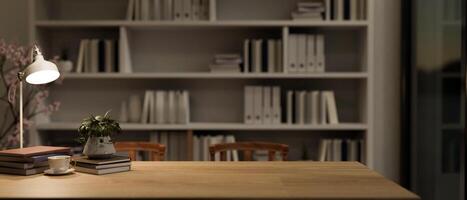 A long wooden table against a large bookshelf in a reading room or office at night. photo