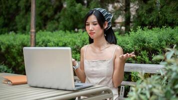 Beautiful Asian woman is having an online meeting with her colleagues, working remotely in a garden. photo