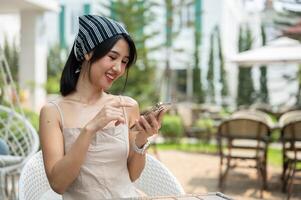 A beautiful Asian woman in a cute dress sits in a beautiful English garden using her smartphone. photo