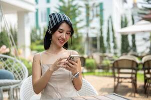 A beautiful Asian woman in a cute dress sits in a beautiful English garden using her smartphone. photo