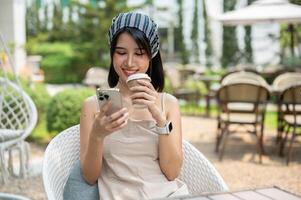 A beautiful Asian woman sits in a beautiful English garden sipping coffee and using her smartphone. photo