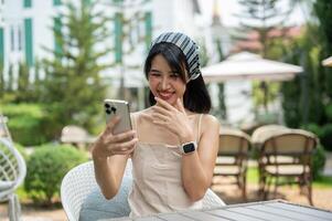 A woman laughs at her phone and enjoys chatting with her friends online while relaxing in a garden. photo