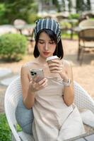 A beautiful Asian woman sits in a beautiful English garden sipping coffee and using her smartphone. photo