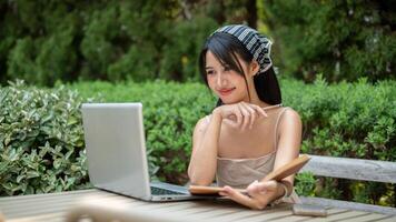 An attractive woman is working remotely in a garden, looking at her laptop, satisfied with her work. photo