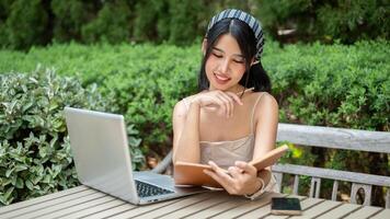 A beautiful Asian woman is working remotely or studying online in a garden, reading a book. photo