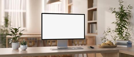 A computer mockup and objects are on a wooden table in a contemporary minimalist co-working space. photo