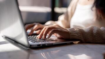 Close-up image of a woman typing on keyboard, working on her laptop computer at a table indoors. photo