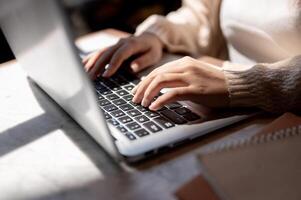 Close-up image of a woman typing on keyboard, working on her laptop computer at a table indoors. photo