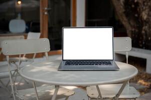 A laptop computer with a white-screen mockup is on an outdoor table of a coffee shop. photo