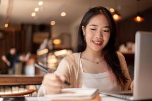 A young positive Asian female college student studying online and doing homework at a coffee shop. photo