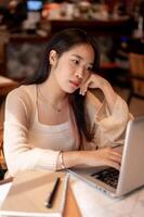 Young bored and tired Asian woman working on her laptop computer at a coffee shop, lack of energy. photo