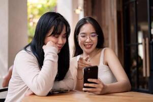 Two happy Asian women are enjoying talking and looking at something on a smartphone together. photo