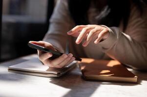 A cropped image of a woman using her smartphone at a table by the window on a sunny day. photo