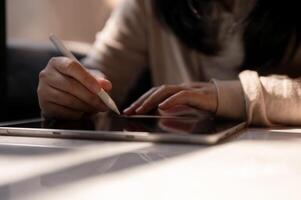 A cropped image of a woman holding a stylus pen, writing on a digital tablet, sitting at a table. photo