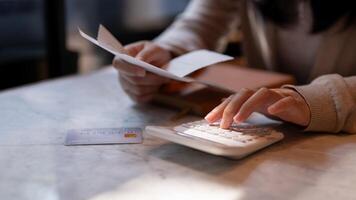 A woman holding receipt and using a calculator, sitting at a table indoors, calculating her expenses photo