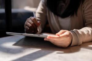 un recortado imagen de un mujer participación un aguja bolígrafo, escritura en un digital tableta, sentado a un mesa. foto
