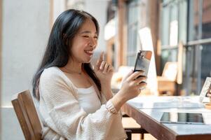 A cheerful Asian woman is laughing and enjoying talking on a call on her smartphone. photo