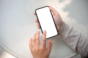 A close-up image of a woman sits outdoors on a sunny day and uses her smartphone, typing on screen. photo