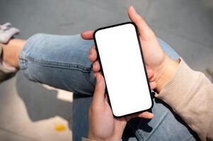 A close-up image of a woman in jeans sits outdoors on a sunny day and uses her smartphone. photo