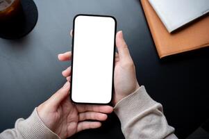 Top view image of a woman holding a smartphone white-screen mockup over an office desk workspace. photo