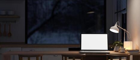 A laptop on a dining table in a contemporary kitchen at night with a dim light from a floor lamp. photo