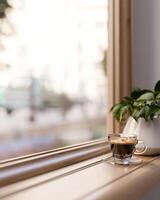 A wooden window sill with a coffee cup and a potted plant in a minimalist living room. photo
