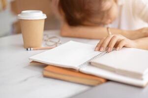 A tired, sleepy young Asian female student falls asleep on the table while doing her homework. photo