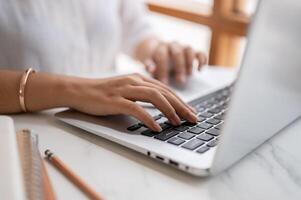 un de cerca imagen de un mujer mecanografía en teclado, trabajando en el computadora a un mesa en un café tienda. foto