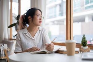 A college student is pondering thinking something while doing her homework in a coffee shop. photo