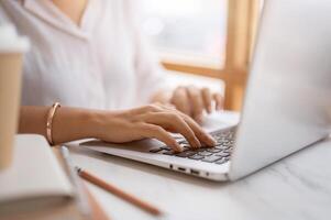 un de cerca imagen de un mujer mecanografía en teclado, trabajando en el computadora a un mesa en un café tienda. foto