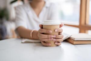 un de cerca imagen de un asiático mujer participación un para llevar café taza, sentado en un café tienda. foto