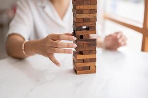 un mujer paga su atención en jugando un de madera bloquear juego a un mesa, Moviente un de madera bloquear. foto