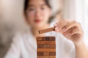 A close-up shot of a woman playing a wooden block game at a table, placing a wooden block on the top photo
