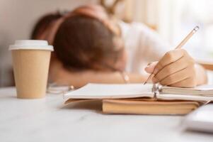 A tired, sleepy young Asian female student falls asleep on the table while doing her homework. photo