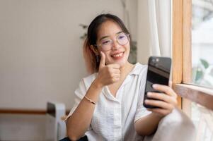 A happy young Asian woman is showing her thumb up while talking on a call on her smartphone. photo