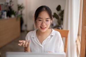 A young Asian woman is talking, having an online meeting while working remotely at a coffee shop. photo