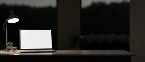 A dark private office or home office at night features a laptop computer mockup on the table. photo