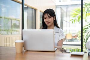 An attractive Asian businesswoman working on her laptop computer in a coffee shop co-working space. photo